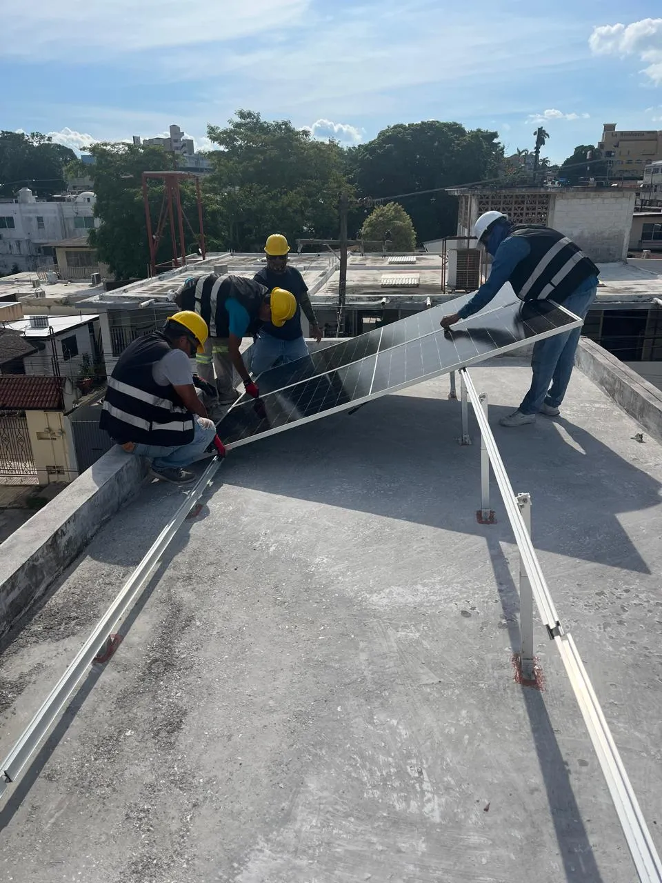 Cuadrilla de Solar Performance con equipo de seguridad instalando un panel solar sobre un techo, con la ciudad de fondo