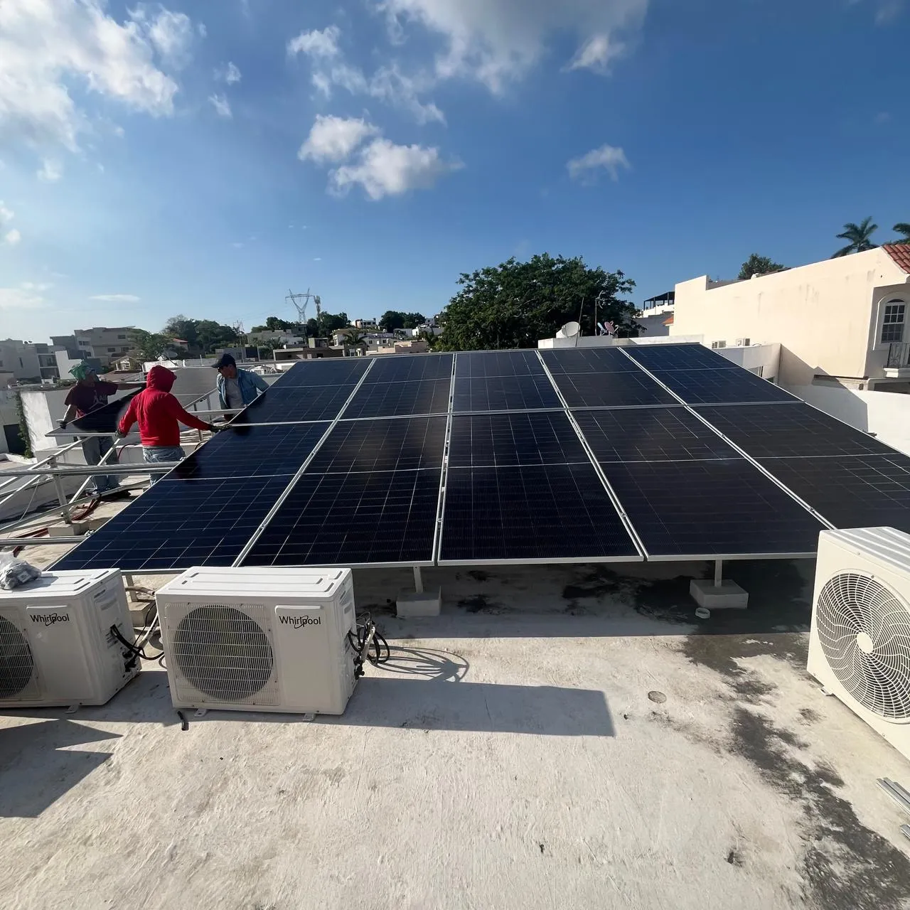Instaladores trabajando en un sistema solar sobre un techo, con la ciudad de fondo